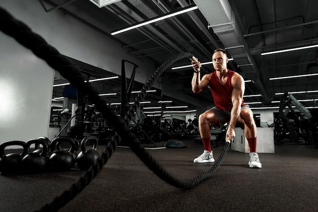 Sport. Strong man exercising with battle ropes at the gym with. Athlete doing battle rope workout at gym. Dramatic sports background.