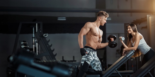 Sport, training, fitness, lifestyle and people concept - young woman with personal trainer flexing back and abdominal muscles on bench in gym