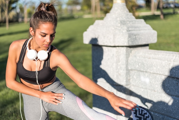 Sport woman doing lawn exercises and stretching on the grass outdoor in a park listening music