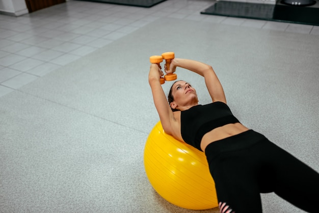 Sport woman exercising with a pilates ball and dumbbells.