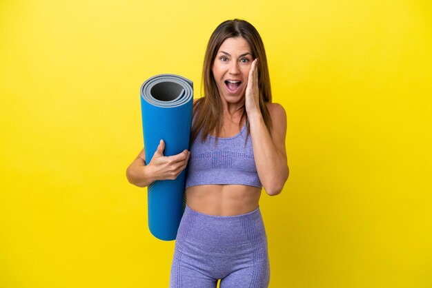 Sport woman going to yoga classes while holding a mat isolated non yellow background with surprise and shocked facial expression