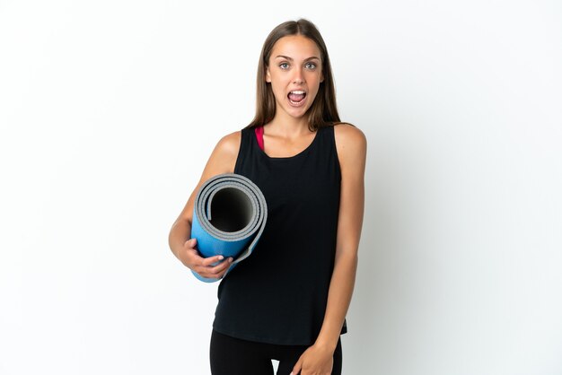 Sport woman going to yoga classes while holding a mat over isolated white background with surprise facial expression