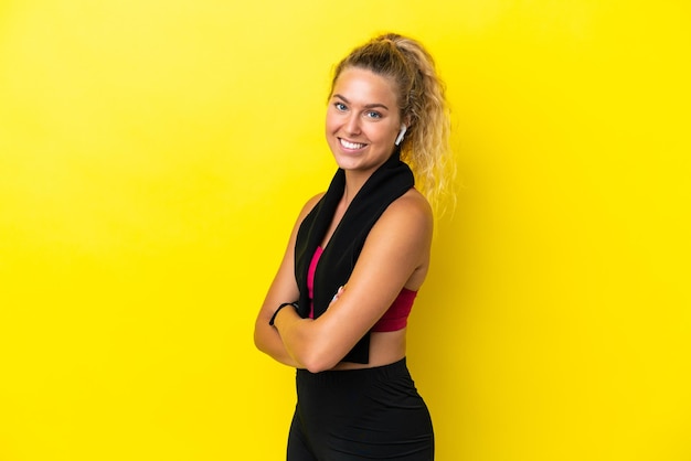 Sport woman with towel isolated on yellow background with arms crossed and looking forward