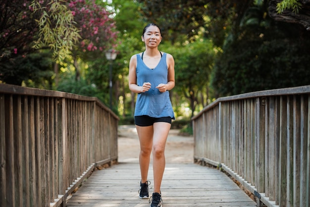 Sport young woman running on a wooden bridge in the park