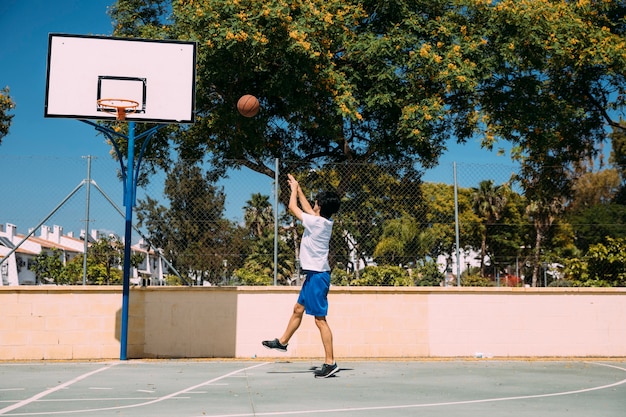 Sportive male throwing ball into hoop on urban background