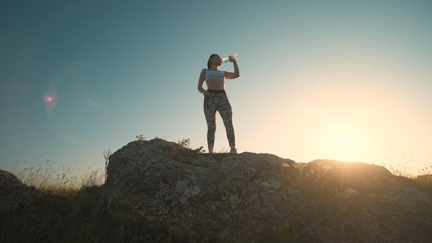 The sportive woman drinking water on a mountain top