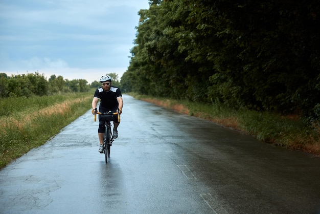 Sportive young bearded man cyclist in uniform helmet and glasses riding bike on road in chill