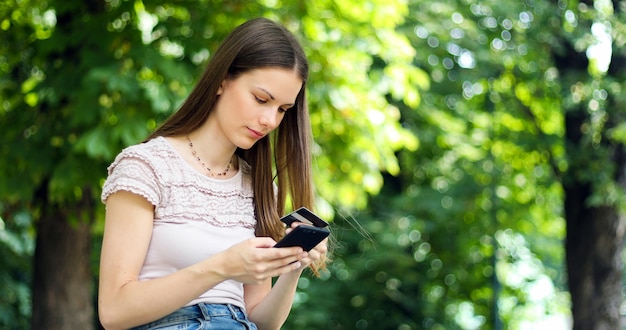 SPortrait of a happy woman paying online with credit card and smart phone in a park