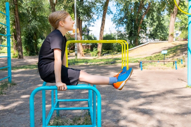 A sports boy holds on to the crossbar with his hands and stretches his legs forward while it is very difficult for him