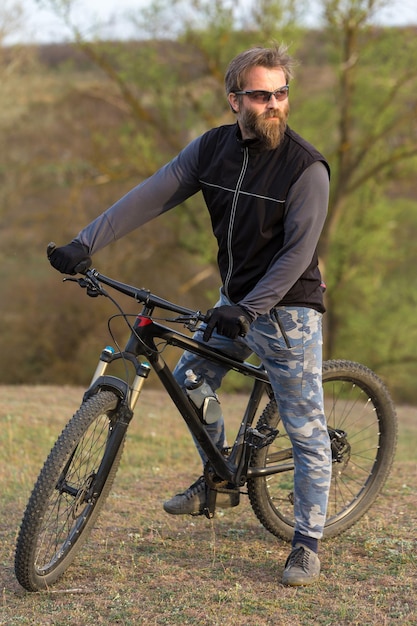 Sports brutal bearded guy on a modern mountain bike Cyclist on the green hills in the spring