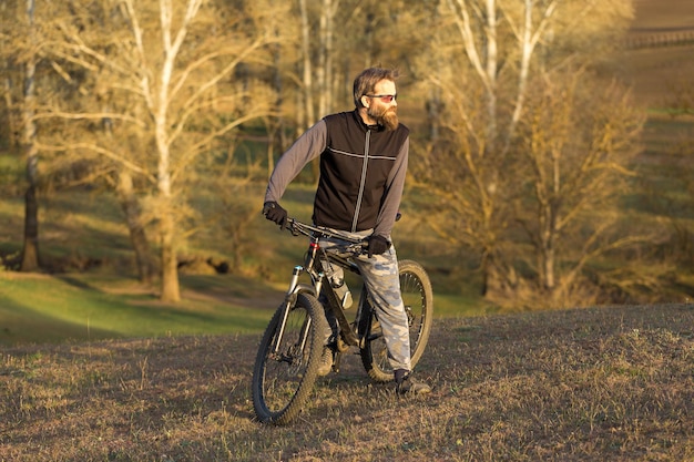 Sports brutal bearded guy on a modern mountain bike Cyclist on the green hills in the spring