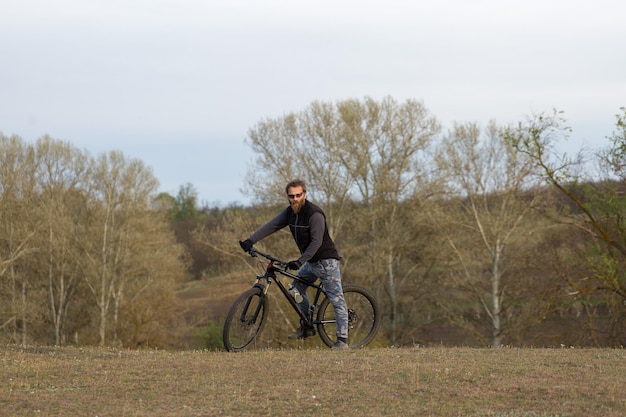 Sports brutal bearded guy on a modern mountain bike Cyclist on the green hills in the spring