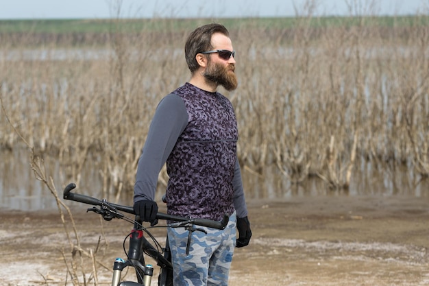 Sports brutal bearded guy on a modern mountain bike A cyclist in a salt deserted place by the lake