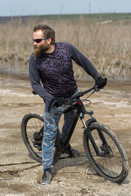 Sports brutal bearded guy on a modern mountain bike A cyclist in a salt deserted place by the lake