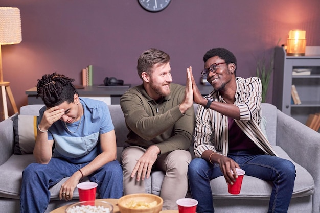 Sports fans high five while watching football match on TV and celebrating goal