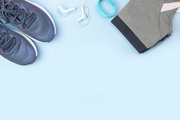 Sports flat layout. Fitness accessories sneakers, clothes, earphones and watches on a blue background. Doing sports and fitness at home.