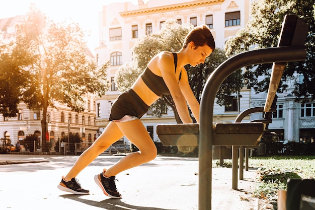 sports girl does push-ups, stands in plank position on even muscular arms on bench on city street