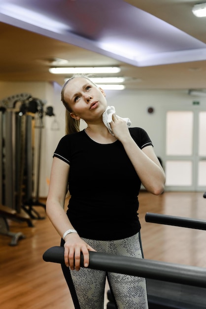 Sports girl in the home gym wipes sweat with a white toweltired woman from workout wiping sweat with towel in sports gym