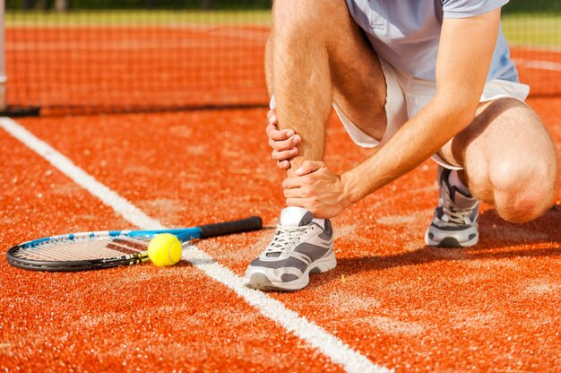 Sports injury. Close-up of tennis player touching his leg while sitting on the tennis court