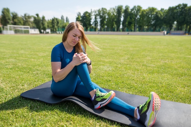 Sports injury of the knee A woman experiences pain in her knee while exercising at a sports stadium healthcare concept