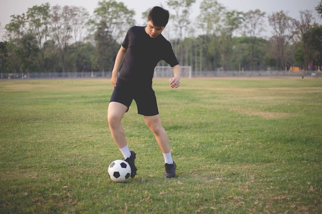 Sports and recreation concept a male soccer player wearing black t-shirt and pants practicing kicking the ball in the grassy field.