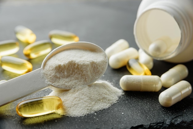 sports supplements close-up with selective focus. Measuring spoon with creatine, omega-3 capsules on a dark background.