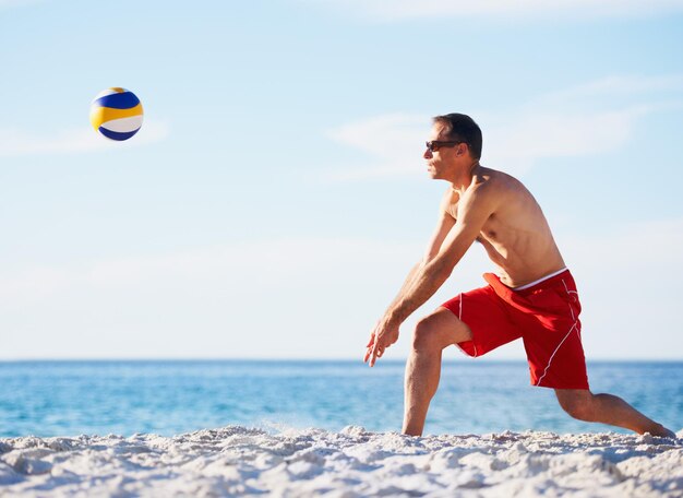 Photo sports volleyball and man at beach with ball serve energy or freedom on blue sky background ocean fitness or male player with handball in nature for cardio workout or athletic game performance