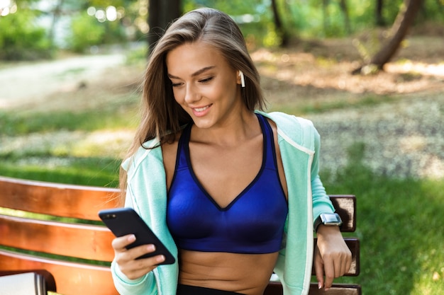 Sports woman in park outdoors listening music with earphones using mobile phone.