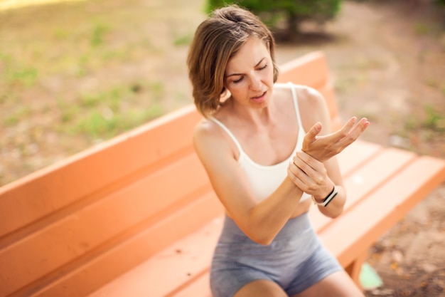 Sports woman with arm pain sitting on the bench in the park. Fitness, healthcare and medicine concept