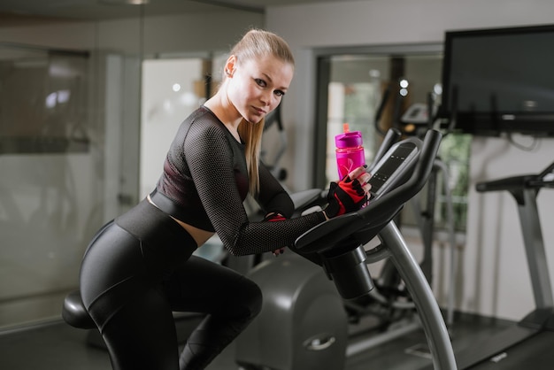 Sports young woman using exercise bike at the gym