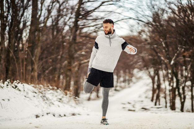 Sportsman doing stretching exercises and preparing to run in nature at snowy winter day. Winter fitness, sport, cold weather