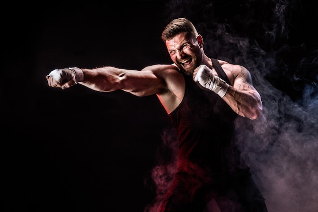 Sportsman muay thai boxer fighting on black wall with smoke.