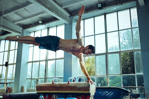 The sportsman performing difficult gymnastic exercise at gym. The sport, exercise, gymnast, health, training, athlete concept. Caucasian fit model