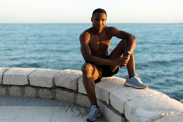 Sportsman sitting on the ocean coast and looking at the camera with pleasure smile