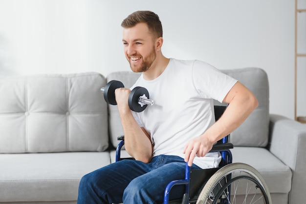 Sportsman sitting in wheelchair and outstretching arms with dumbbells during rehabilitation exercise in modern medical center Man sitting on wheelchair at home