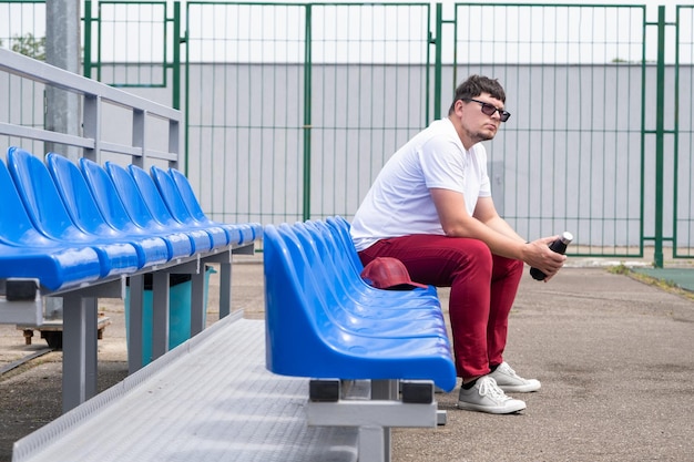 sportsman with a bottle of water sitting and resting at the seats at the stadium