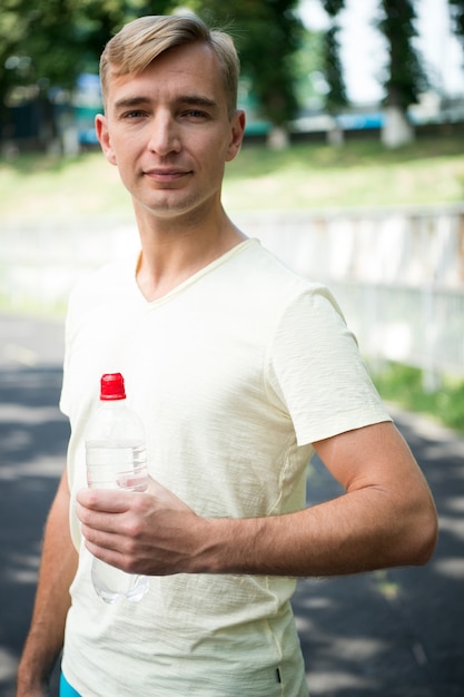 Sportsman with plastic bottle on sunny outdoor. Thirsty man with water bottle on stadium. Thirst and dehydration. Drinking water for health. Sport activity and energy.