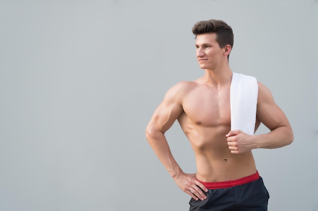 Sportsman with towel on neck on grey background. Man with bare torso with six pack and ab. Athlete with strong arms, biceps and triceps. Fitness and sport. Hygiene and health concept.