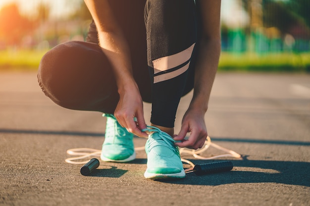 Sportswoman is tying shoelaces on sneakers and is preparing to jump rope outdoors