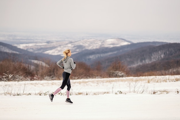 Sportswoman running in nature on snowy path at winter. Healthy lifestyle, winter fitness, cold weather