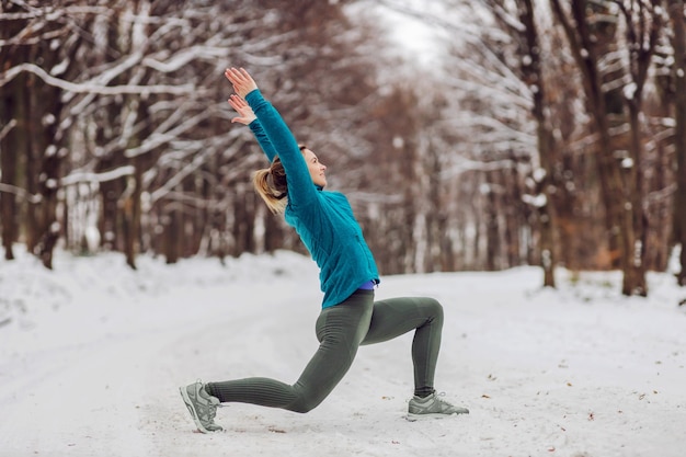 Sportswoman in warm outfit doing yoga exercises in snowy forrest. Fitness outdoors, snow, cold, winter yoga