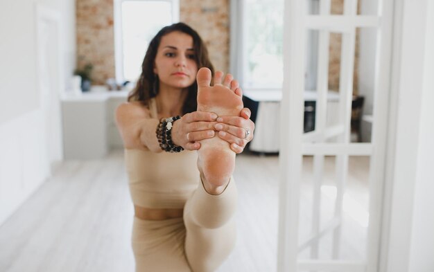 Photo a sporty beautiful girl does yoga exercises standing with her leg stretched out, stretching the spine, shoulders, hamstrings. close-up of the foot