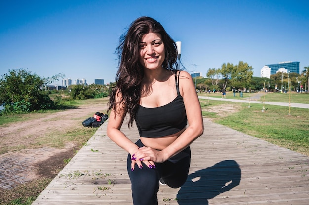 Sporty caucasian latin woman stretching legs looking at camera and smiling