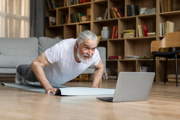 Sporty elderly man planking at home watching fitness video