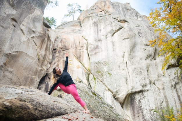 Sporty fit woman is practicing yoga on the boulder in the nature