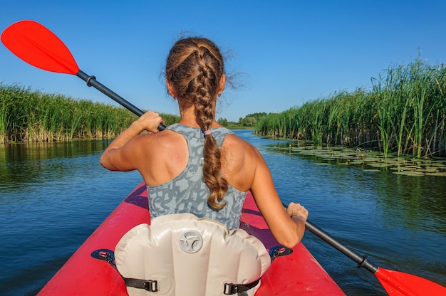 A sporty girl in a red kayak paddles along the Zdvizh River. Ukraine