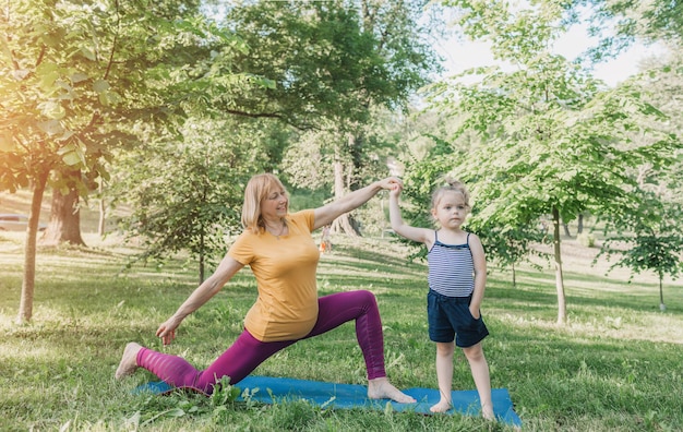 A sporty grandmother exercises with her granddaughter in the park on a gym mat. a sporty lifestyle.