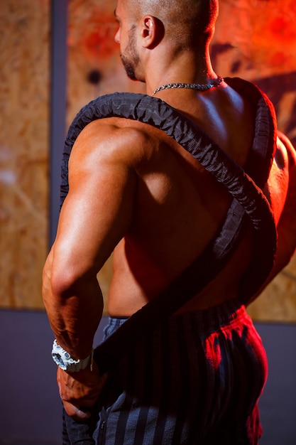 Sporty handsome strong man posing with sports rope on the background of the gym. A strong bodybuilder with perfect abs, shoulders, biceps, triceps and chest.