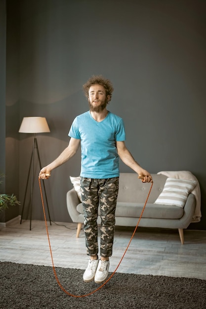 Sporty male jumping rope in fast rhythm on the carpet in his living room he finds of sport