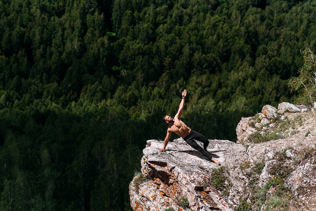 Photo a sporty man does yoga. a healthy lifestyle. the concentration of the body. a man does yoga in the mountains. a man does yoga on a rock. a man meditates in nature. meditation in the mountains